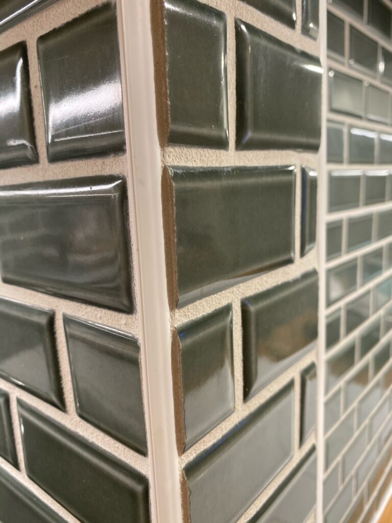 Detail view of green beveled subway tile meeting at an outside corner with tight grout lines and metal trim