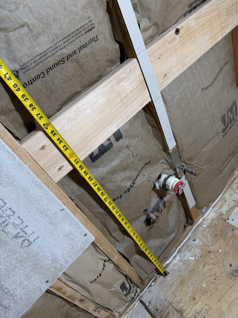 Tape measure spanning studs during bathroom renovation framing and measurement