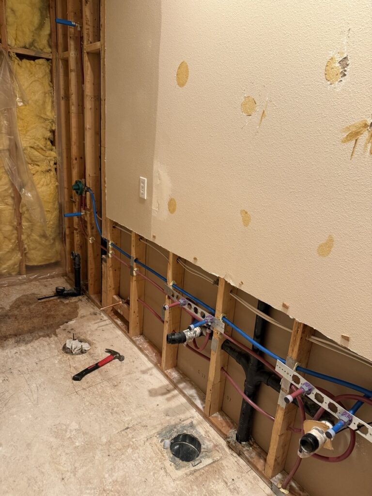 Interior wall stripped to studs with new PEX water lines in red and blue and ABS drain plumbing rough-in