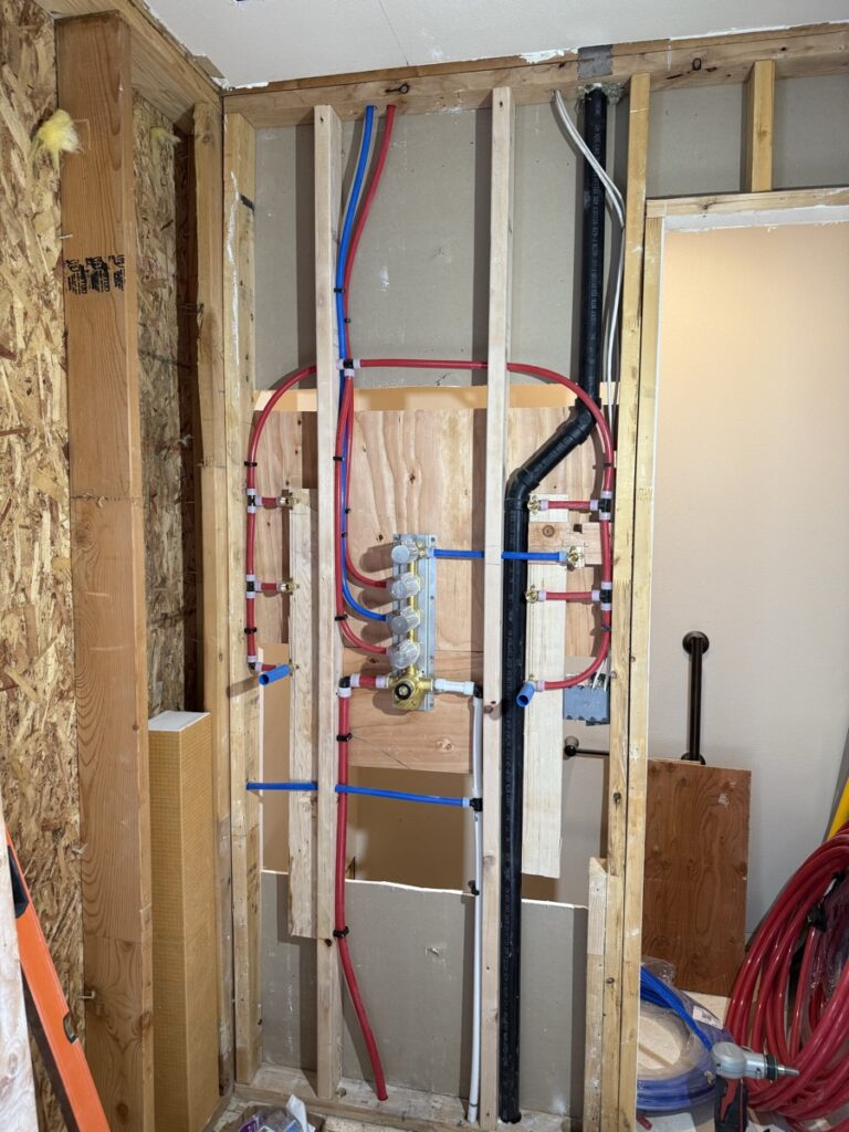Multi-zone PEX plumbing manifold installed at a stud wall during new construction rough-in