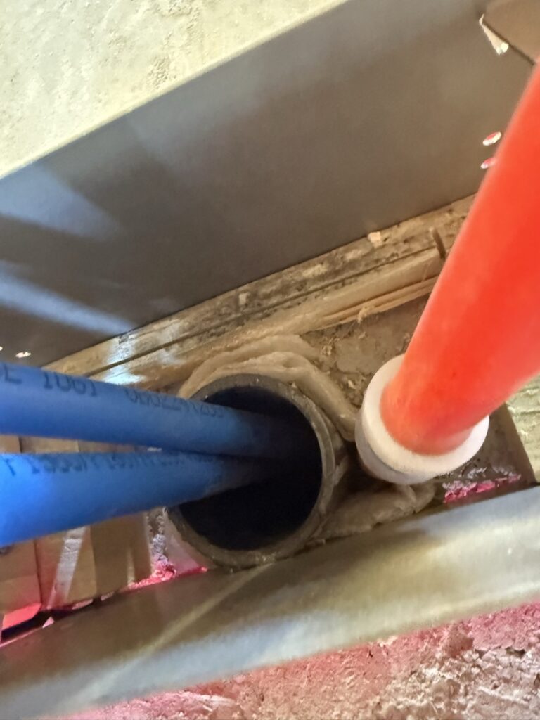 Drain stack penetrations sealed with fire-rated collars through a subfloor, PEX and ABS lines running through