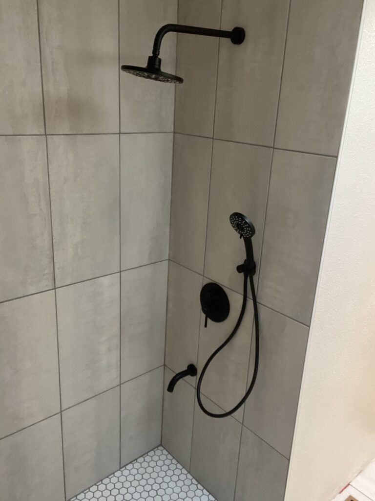 Finished walk-in shower with large-format gray tile walls, white hex mosaic floor and matte black fixtures