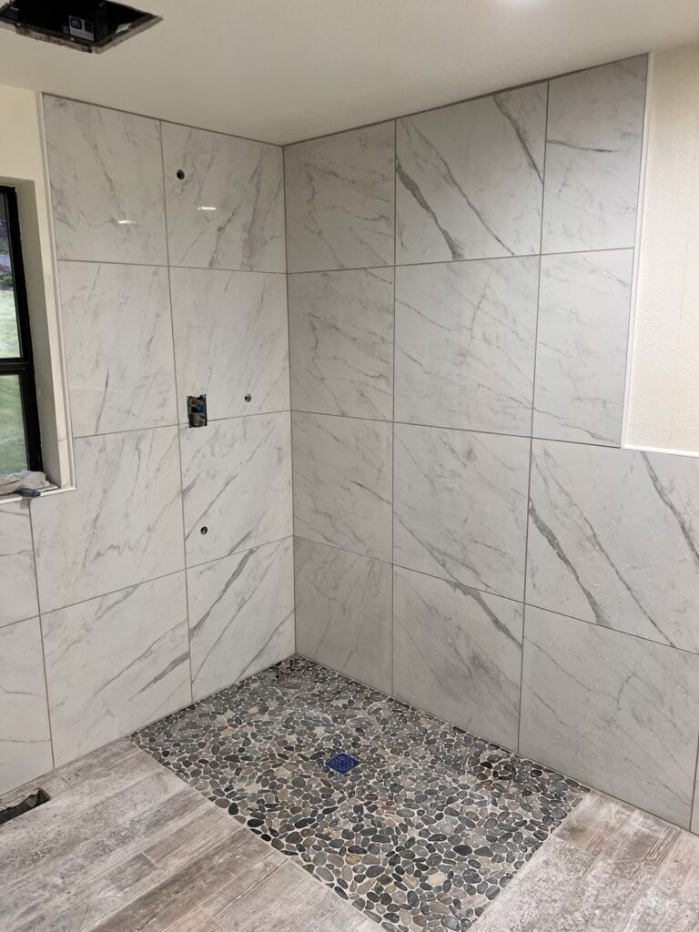 Finished barrier-free walk-in shower with marble-look porcelain walls and river-rock pebble drain area