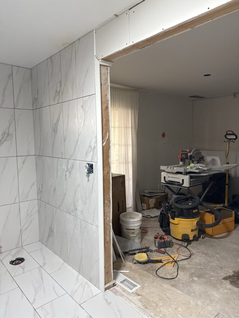 On-site tile installation workspace with wet saw, DeWalt tools and the marble-look shower in background