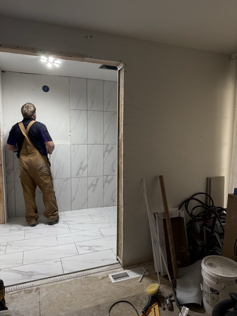 Contractor installing marble-look wall tile in a walk-in shower, hand-setting each piece