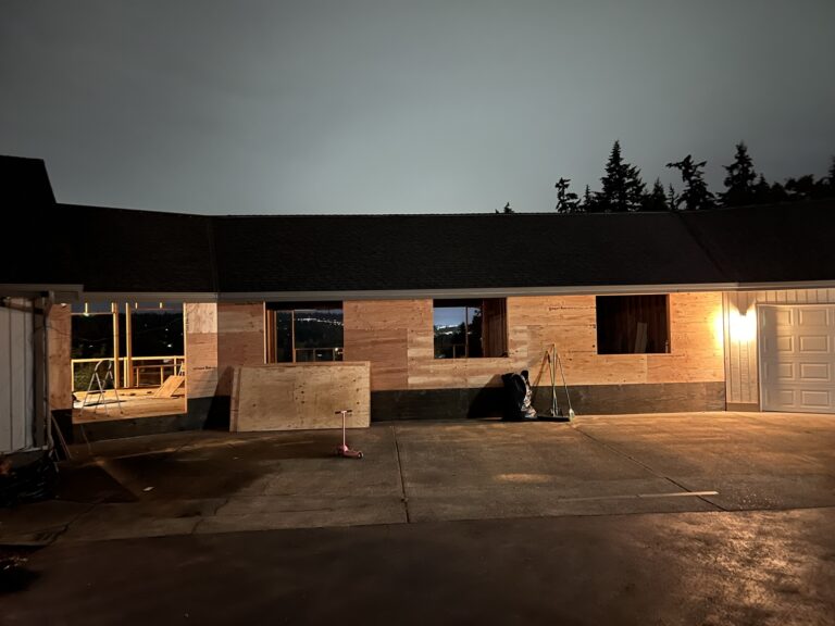 Former garage and carport openings framed and sheathed at dusk, with new window rough-openings cut into the wall