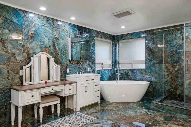 Master bathroom with blue quartzite walls, vintage white vanity with tri-fold mirror and freestanding tub