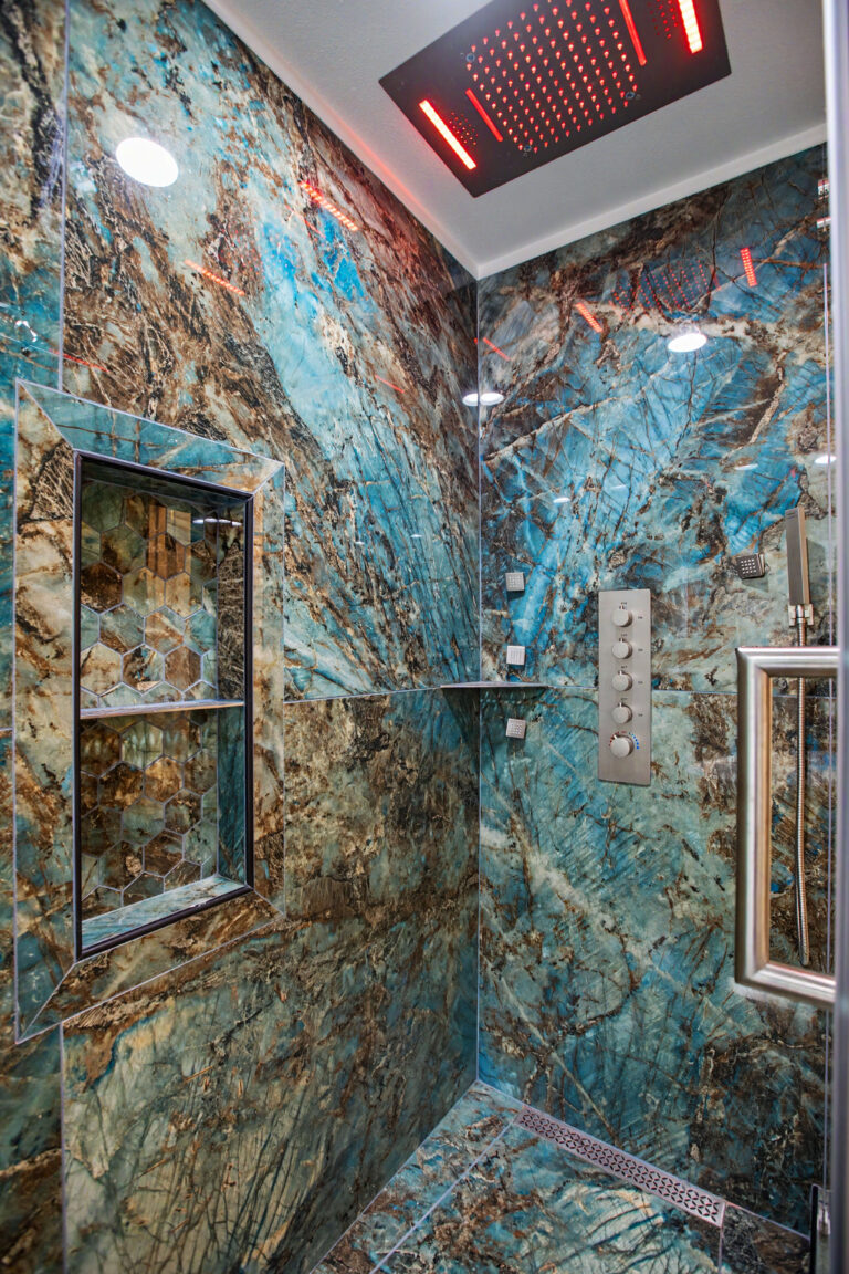 Custom walk-in shower interior with blue quartzite slab walls, chromotherapy rainfall head, digital body jets and niche