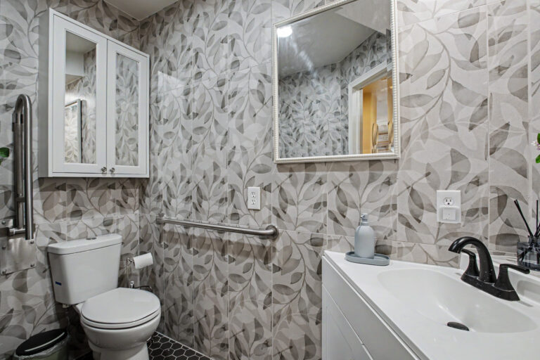 ADA-accessible bathroom with botanical-pattern tile walls, grab bars, barrier-free vanity and medicine cabinet